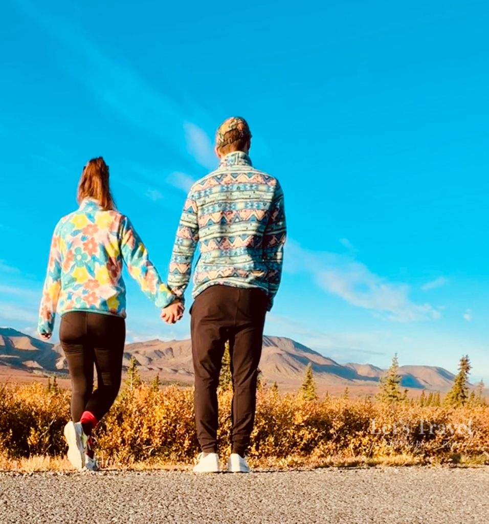 Couple walking hand in hand in Denali National Park Alaska with mountain landscape and blue sky