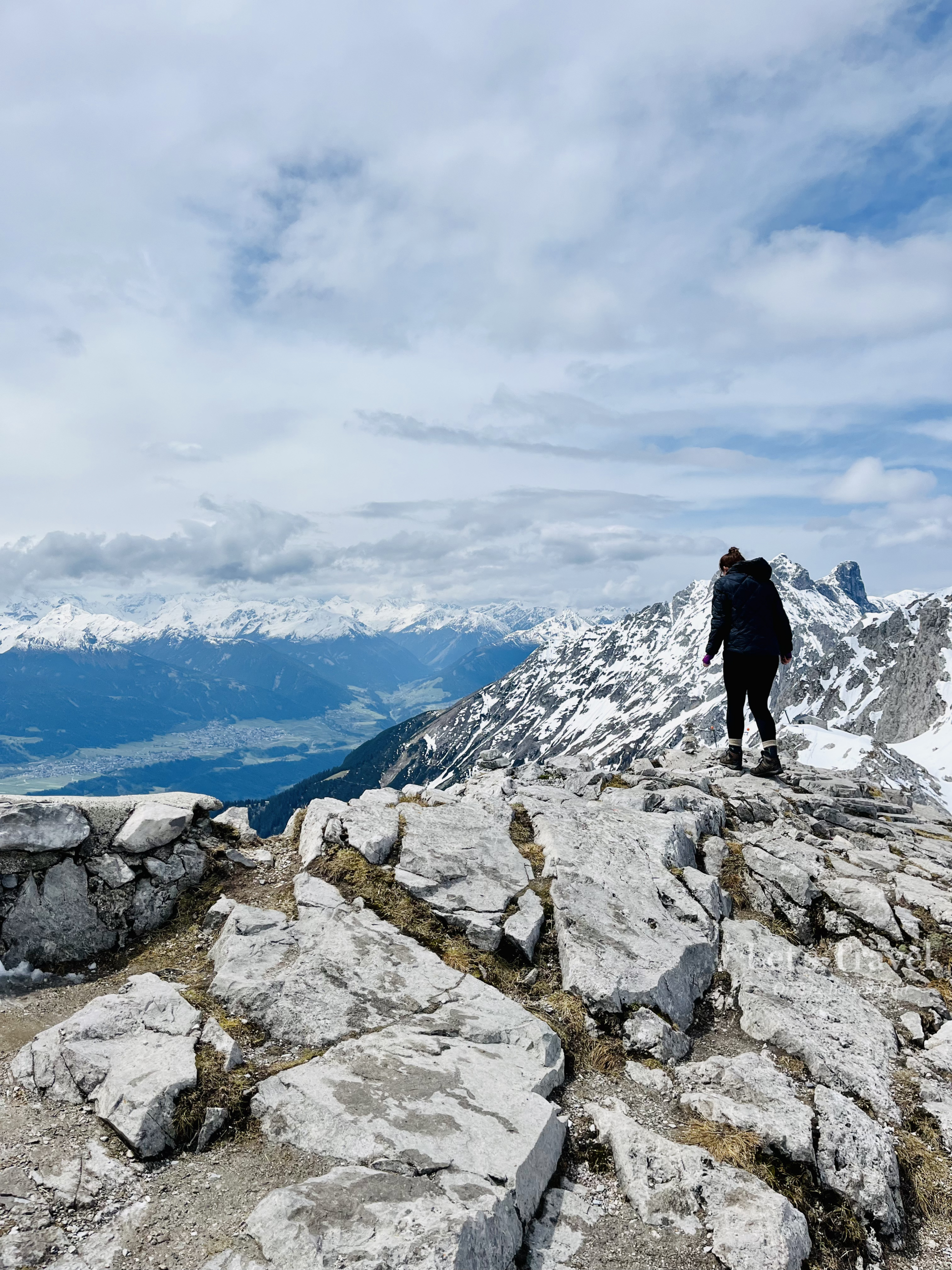 Hiker standing on rocky mountain ridge in Austria with snowy Alps and valley view