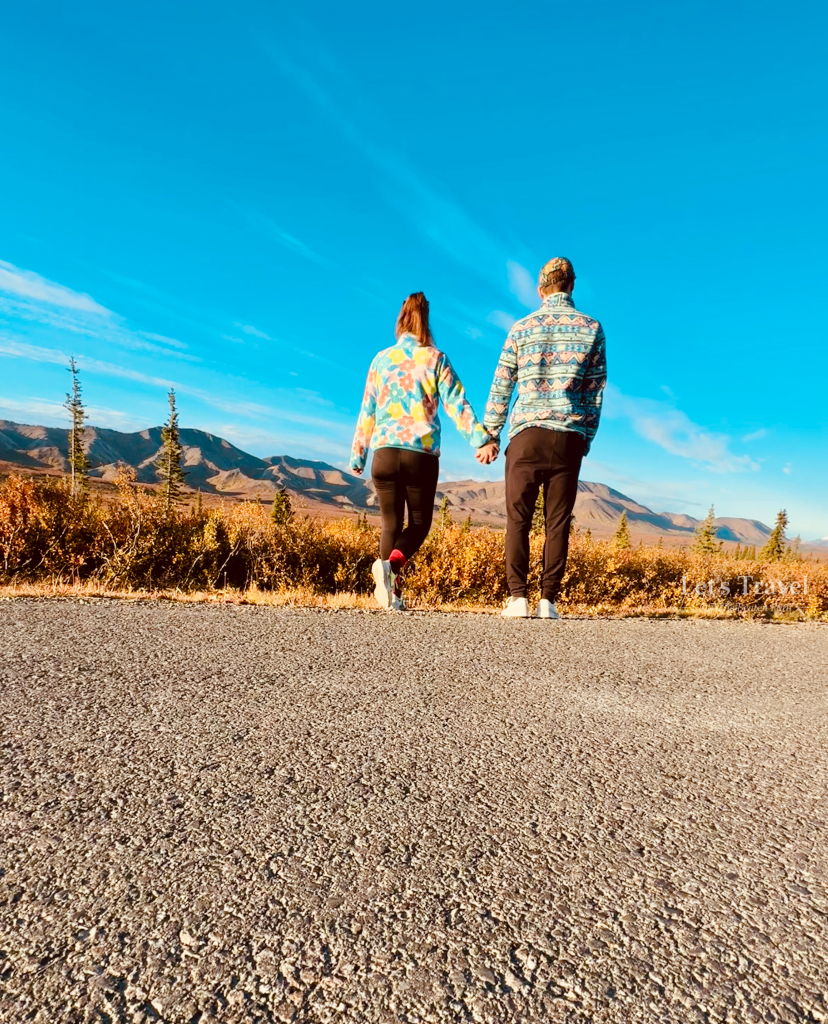 Couple walking hand in hand in Denali National Park Alaska with mountain landscape and blue sky