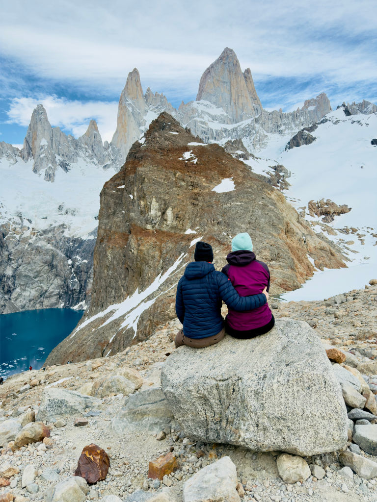 Couple sitting on a rock overlooking Laguna de los Tres with Mount Fitz Roy in Los Glaciares National Park near El Chaltén, Patagonia, Argentina.