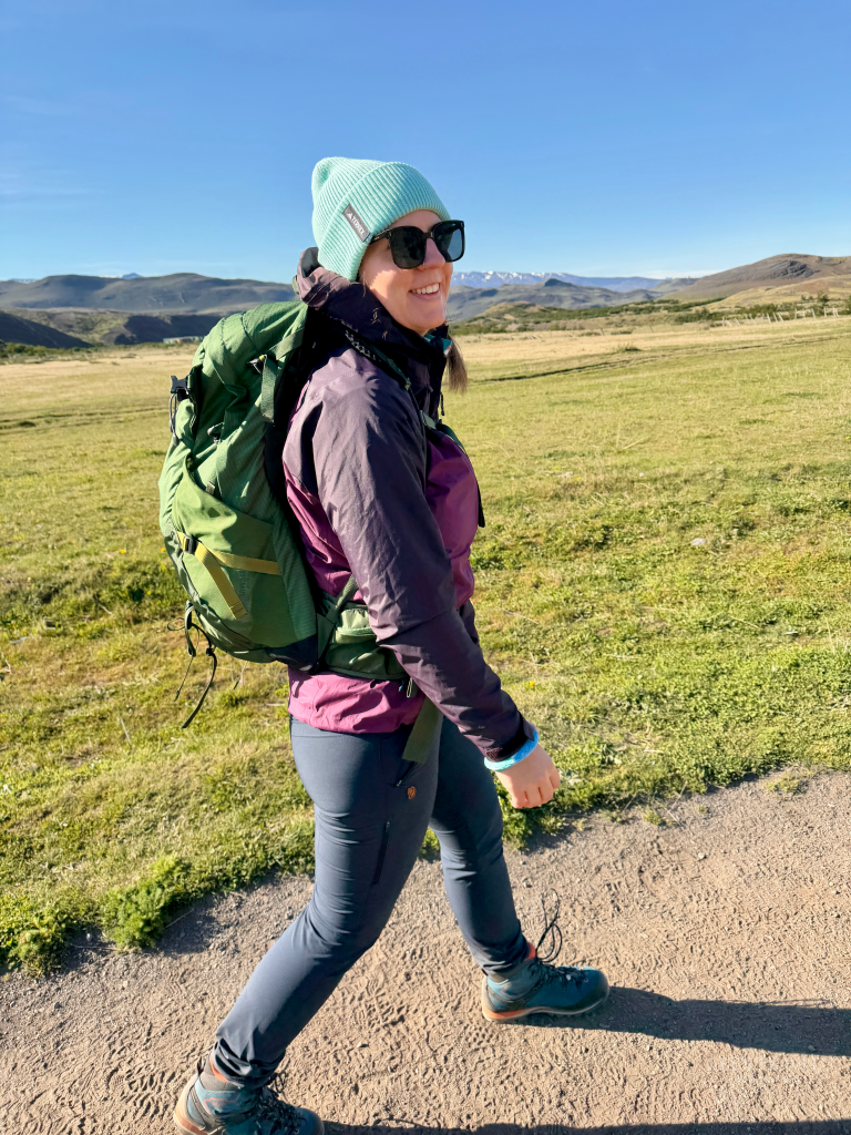 Hiker walking through the grasslands of Torres del Paine National Park in Chilean Patagonia with mountains in the background.