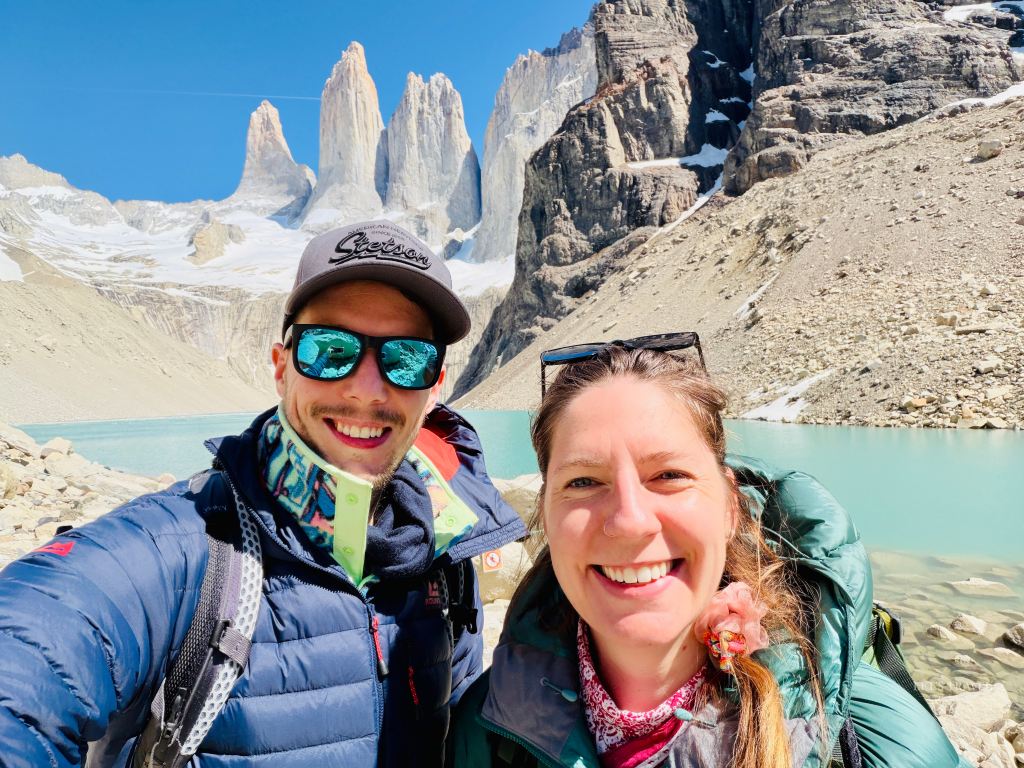 Two hikers taking a selfie at the Base Torres viewpoint in Torres del Paine National Park, Chile, with the iconic granite towers and glacial lake in the background.