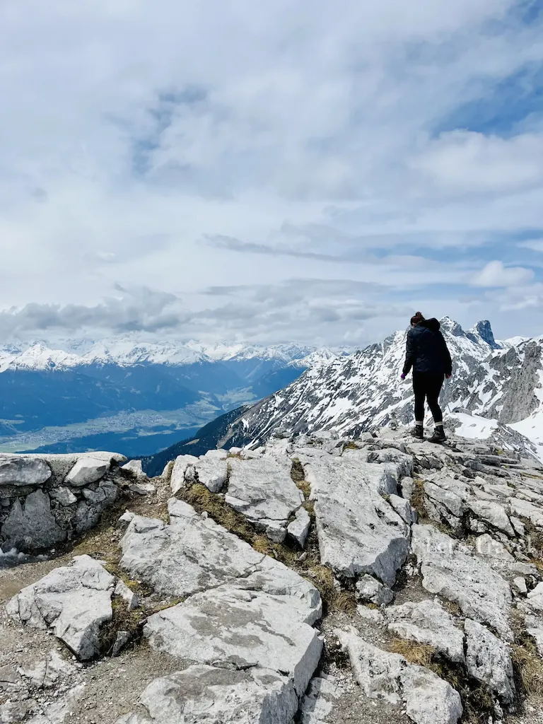 Hiker standing on rocky mountain ridge in Austria with snowy Alps and valley view