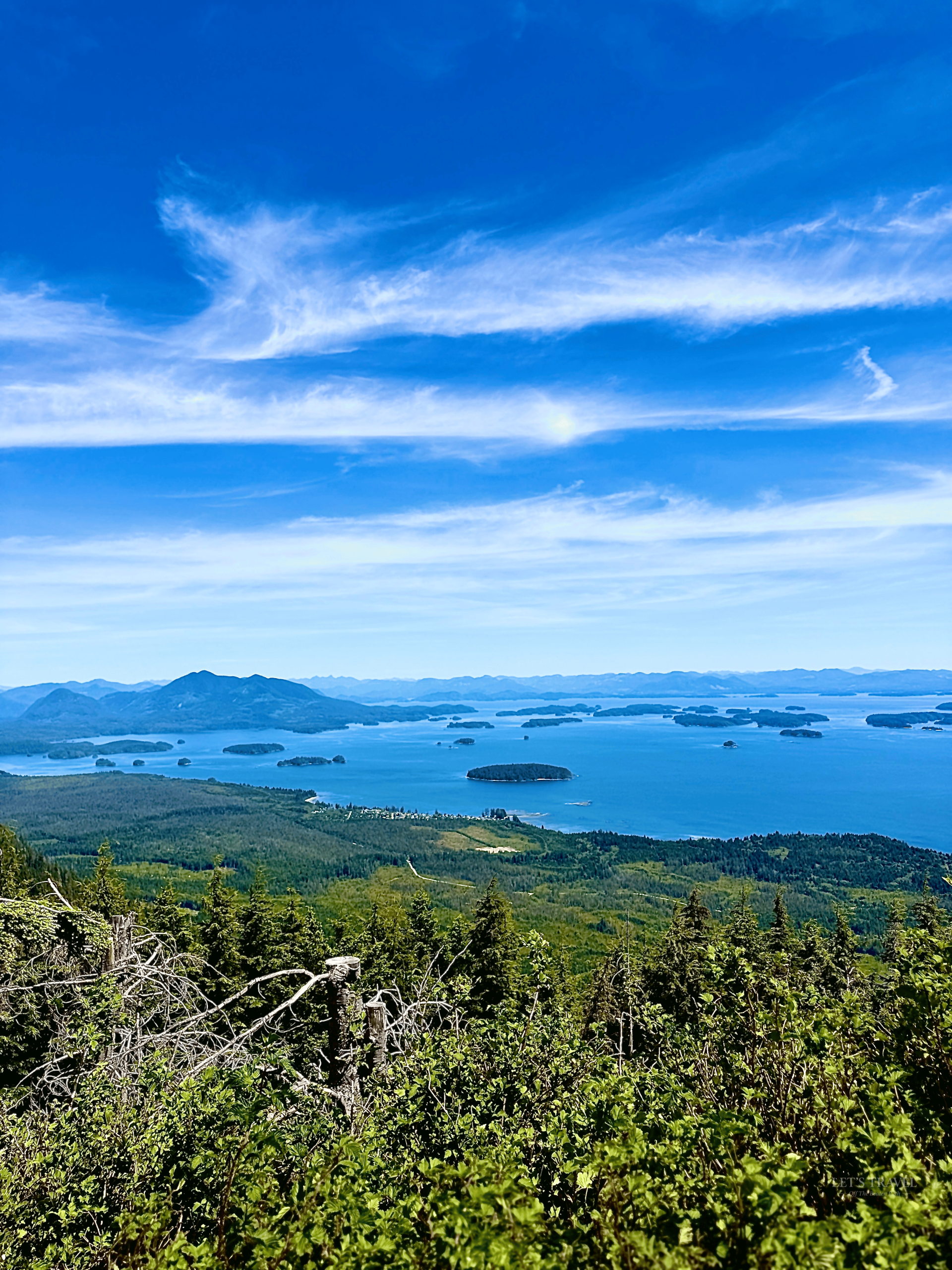 Panoramic view from Mount Ozzard Hike on Vancouver Island, overlooking forested hills, blue coastal waters, scattered islands and distant mountains.
