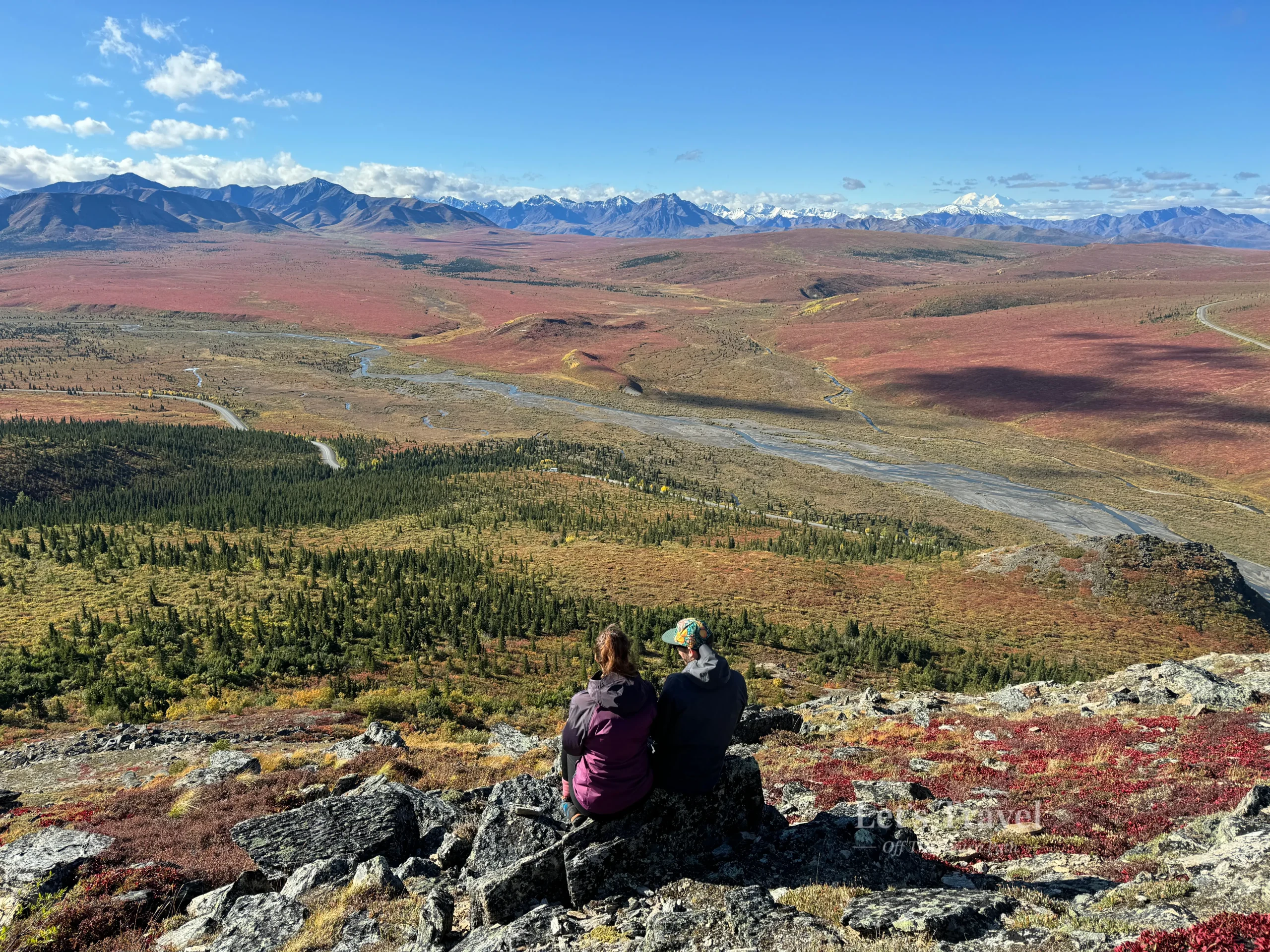 Off the beaten path travel in the mountains. A Couple overlooking vast tundra landscape in Denali National Park Alaska with mountains and river valley